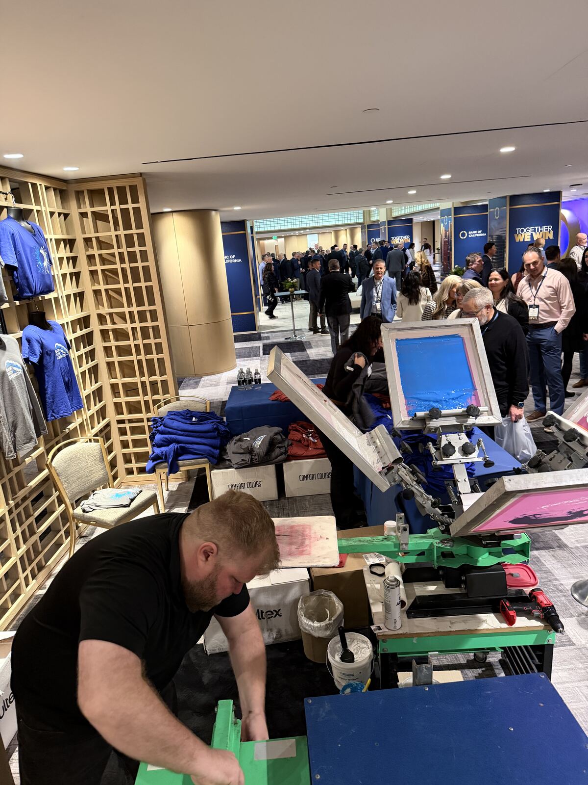 Live event printing demo at a conference booth with staff operating heat press equipment and customers watching
